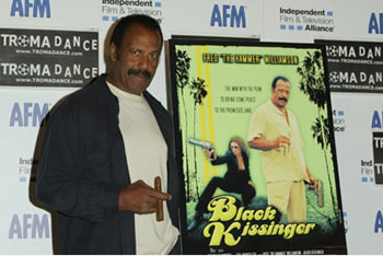 Fred Williamson stands next to a poster for his movie Black Kissinger