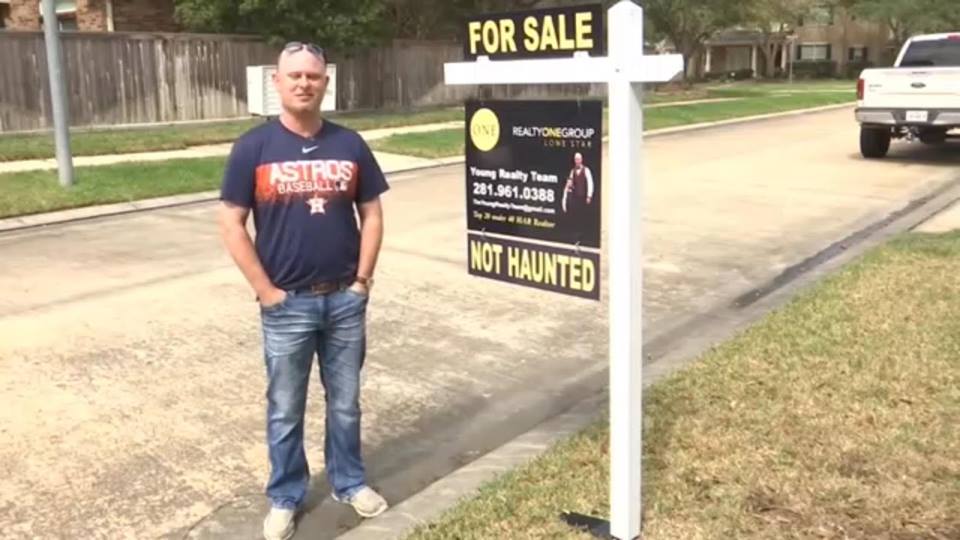 Realtor standing next to a sign that says "For sale: not haunted"