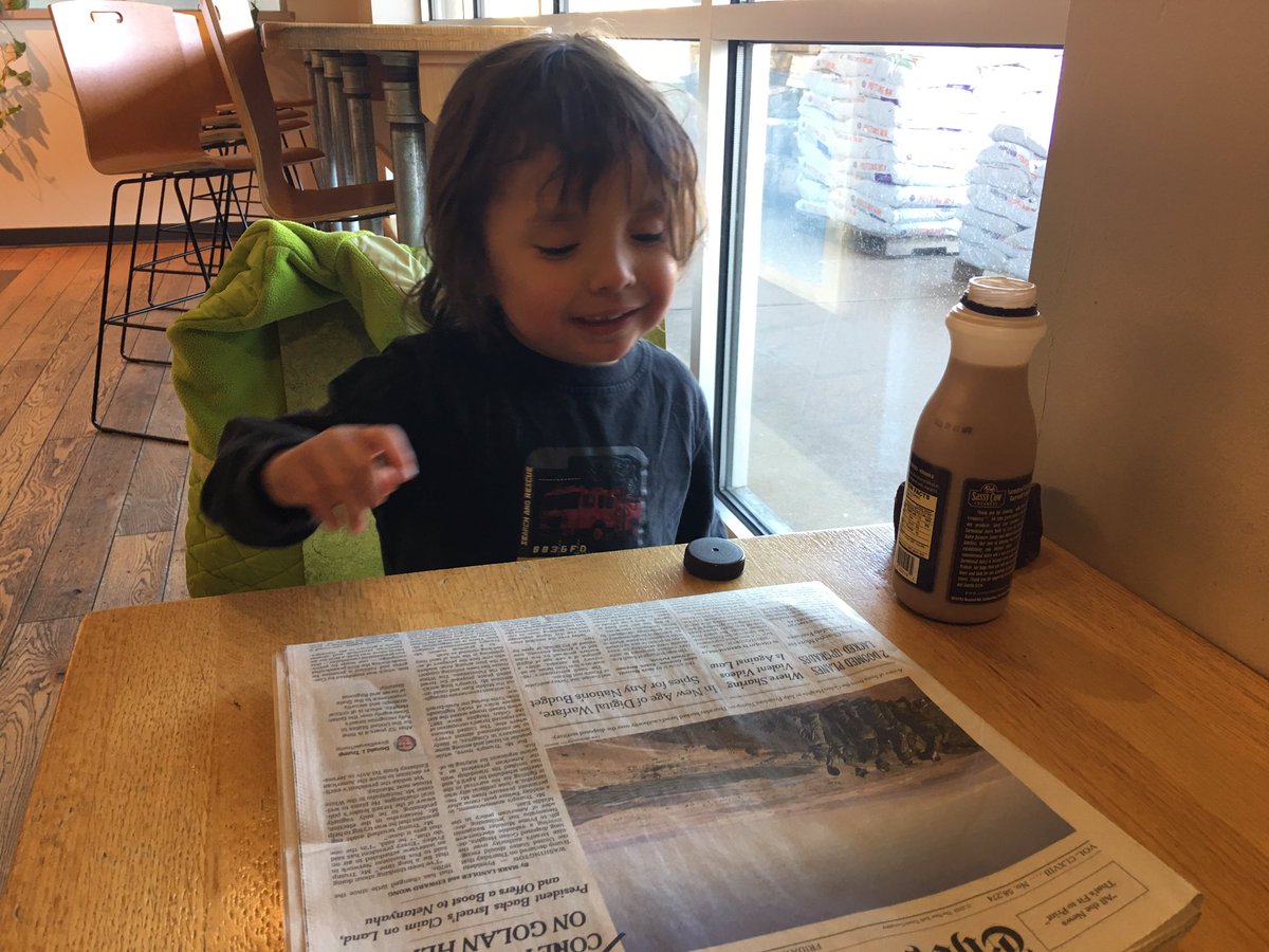 Four year old drinking chocolate and reading the newspaper