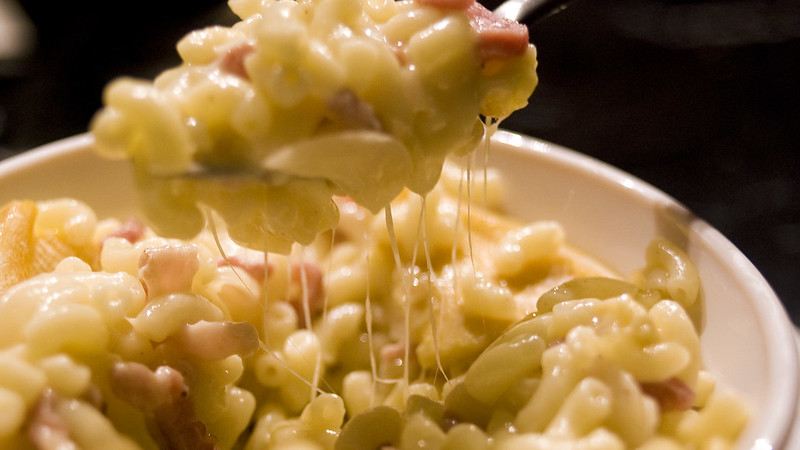 A metal spoon lifts some mac and cheese out of a white bowl. (Photo by Tavallai via Flickr/Creative Commons https://flic.kr/p/95Lw1G)