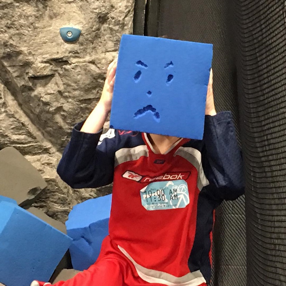 Seven year old holds up a big foam block with a grumpy face on it