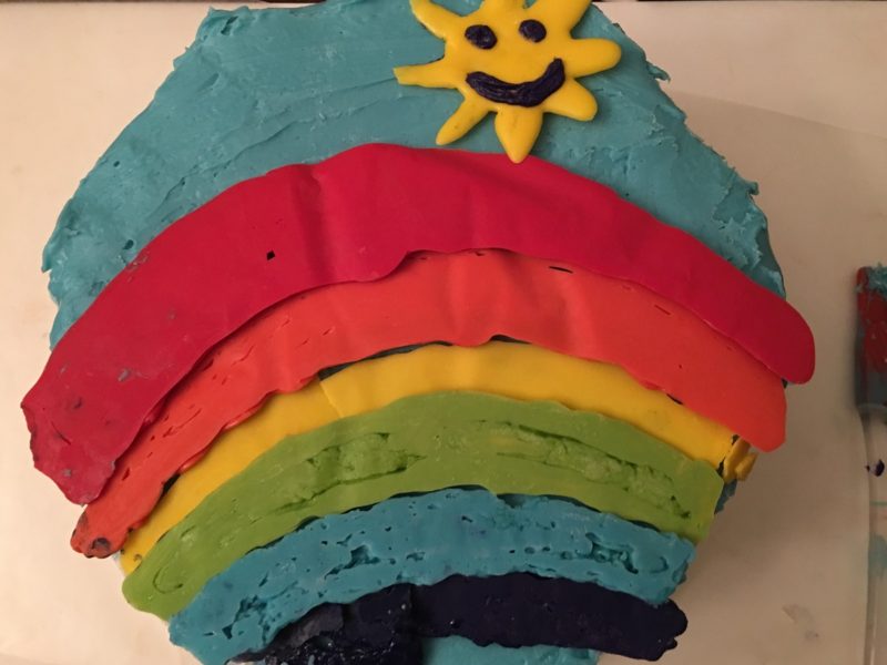 Two layer cake with a rainbow and a smiling sun on it