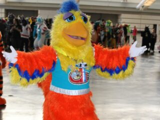 Close up of the San Diego Chicken extending its arms at an event in 2015. (Photo by Douglas Muth via Flickr/Creative Commons, adapted from the original https://flic.kr/p/wMPXvB)