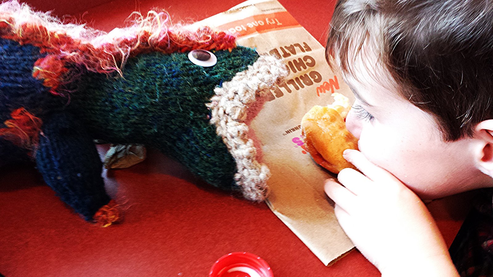 The boy and his toy T-rex eat a doughnut