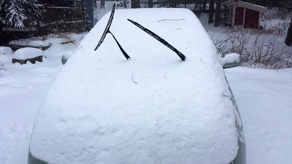Snow covering all of a car except the windshield wipers