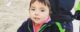 Three year old is wearing a grown-up-sized glove on his left hand and holding it up for the camera