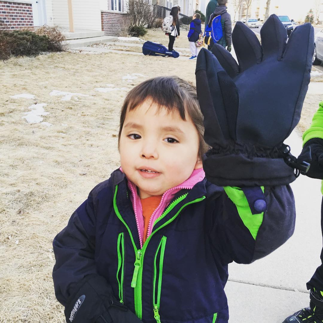 Three year old is wearing a grown-up-sized glove on his left hand and holding it up for the camera