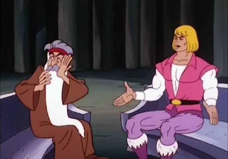 Zagraz, a wizard with a long white beard, clutches his face while sitting next to Prince Adam