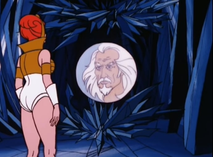 Teela talks with the Oracle, which is the head of an old guy with long white hair and a white goatee inside a large crystal ball