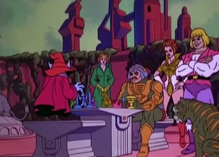Orko plays chess with Man-at-Arms, while Queen Marlena, Teela, Prince Adam and Cringer look on.
