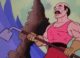 A muscular white man, with a black mustache and a pink t-shirt, holds a garden hoe. He looks surprised and scared, knowing that Skeletor is attacking him.