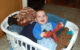 Smiling baby boy and his stuffed bear sitting in a white basket full of laundry.