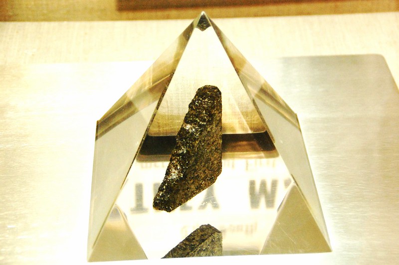 A dark grey rock inside a clear pyramid.