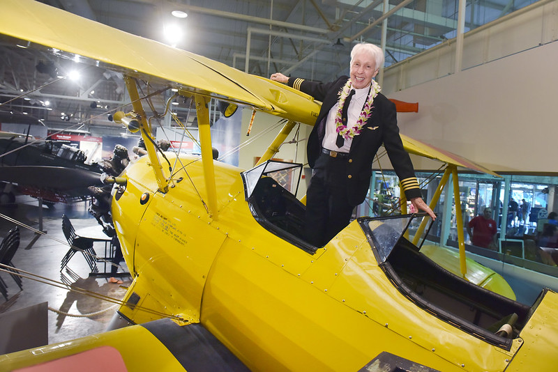 Wally Funk stands and smiles inside a yellow open cockpit airplane. (Photo by Pearl Harbor Aviation Museum via Flickr/Creative Commons https://flic.kr/p/24RSeTv)