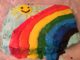 A sky blue sheet cake with a smiling yellow sun in the upper left corner and a large rainbow made of frosting.