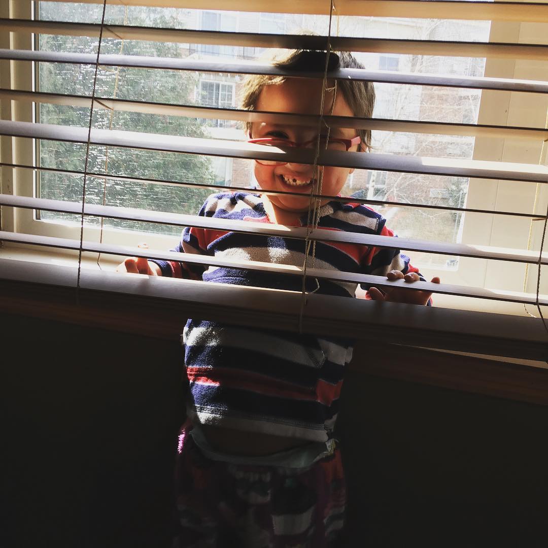 Three year old is hiding behind some vertical blinds and giggling because he's pretending no one knows where he is.