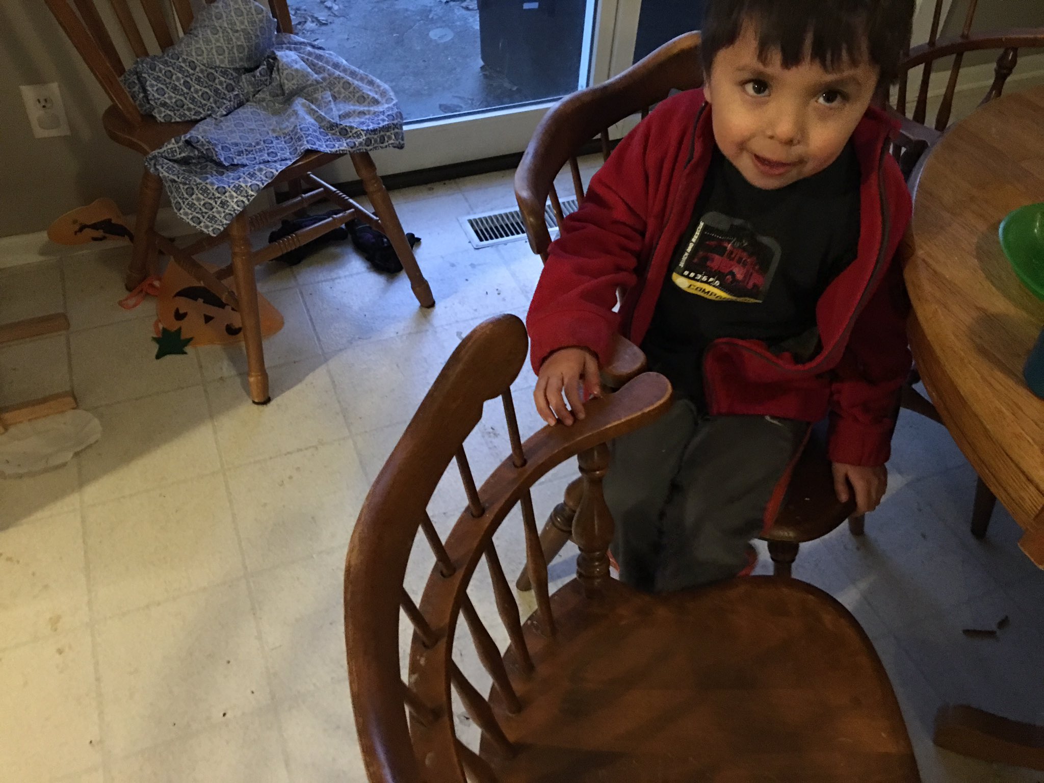 Four year old has his legs "trapped" between two wooden dining room chairs.