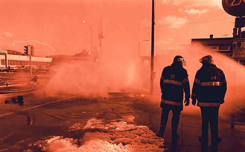 Two firefighters talking outside at a work site. (Photo by starmanseries via Flickr/Creative Commons https://flic.kr/p/cigmGU)
