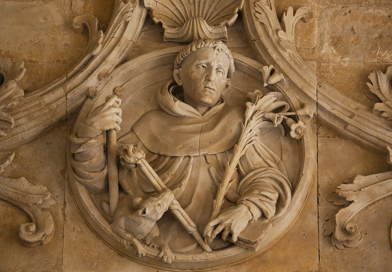 Detail of a relief in the Dominican priory of San Estaban, Salamanca, showing a dog with a lit flare in its mouth by St. Dominic. (Photo by Lawrence OP via Flickr/Creative Commons https://flic.kr/p/a9U7Zd)