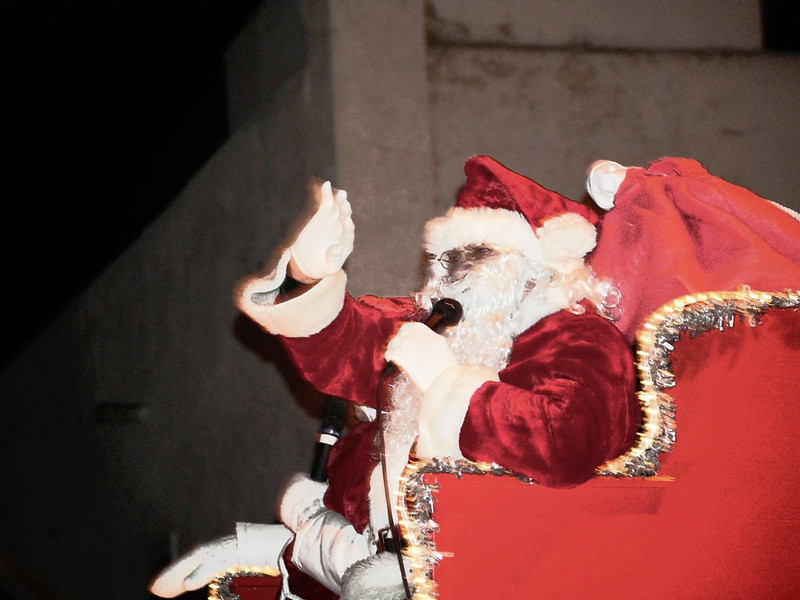 A Santa Claus holds a microphone while sitting in a big red sleigh. Photo by Dwayne via Flickr/Creative Commons https://flic.kr/p/47q6MK