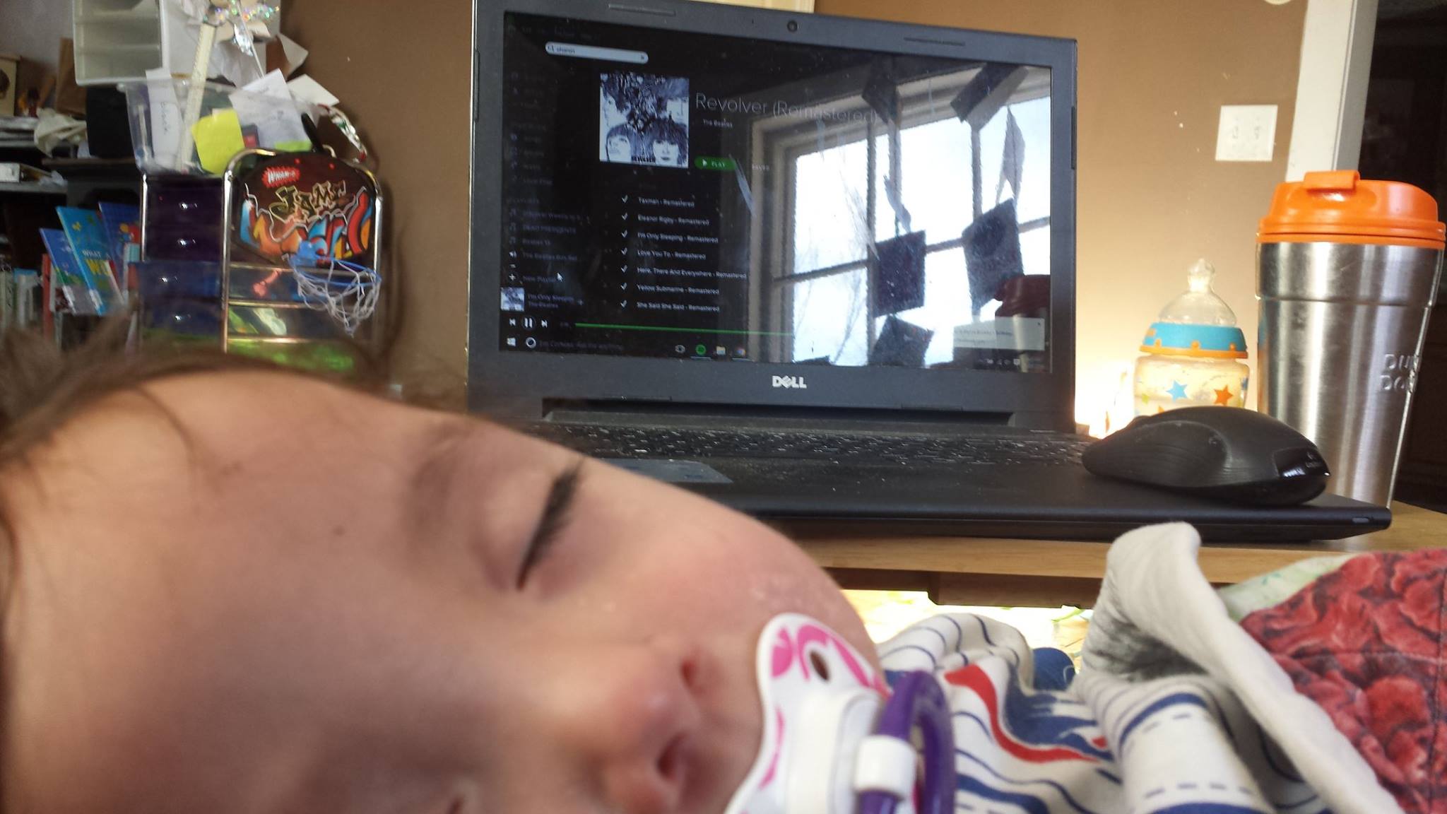 Baby boy is sleeping while the laptop screen shows "I'm Only Sleeping" by The Beatles is playing