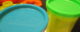 Several yellow cans of Play-Doh; one has a light blue top and the other has a lime green top. (Photo by Kevin Spencer via Flickr/Creative Commons https://flic.kr/p/7e5yza)