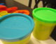 Several yellow cans of Play-Doh; one has a light blue top and the other has a lime green top. (Photo by Kevin Spencer via Flickr/Creative Commons https://flic.kr/p/7e5yza)