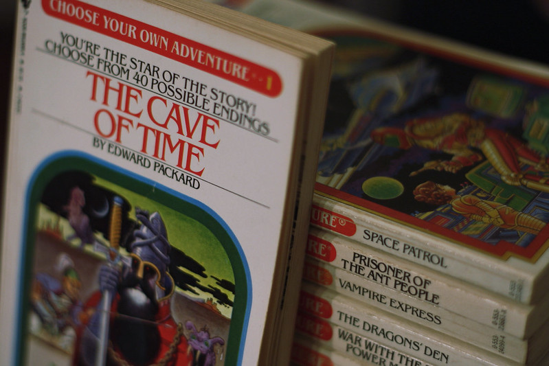 A stack of Choose Your Own Adventure books, with The Cave of Time in a featured position. (Photo by Derek Bruff via Flickr/Creative Commons https://flic.kr/p/aHes9K)