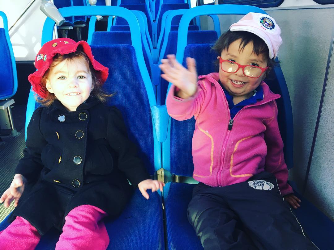 Two year old and three year old smile and wave as they ride the city bus.