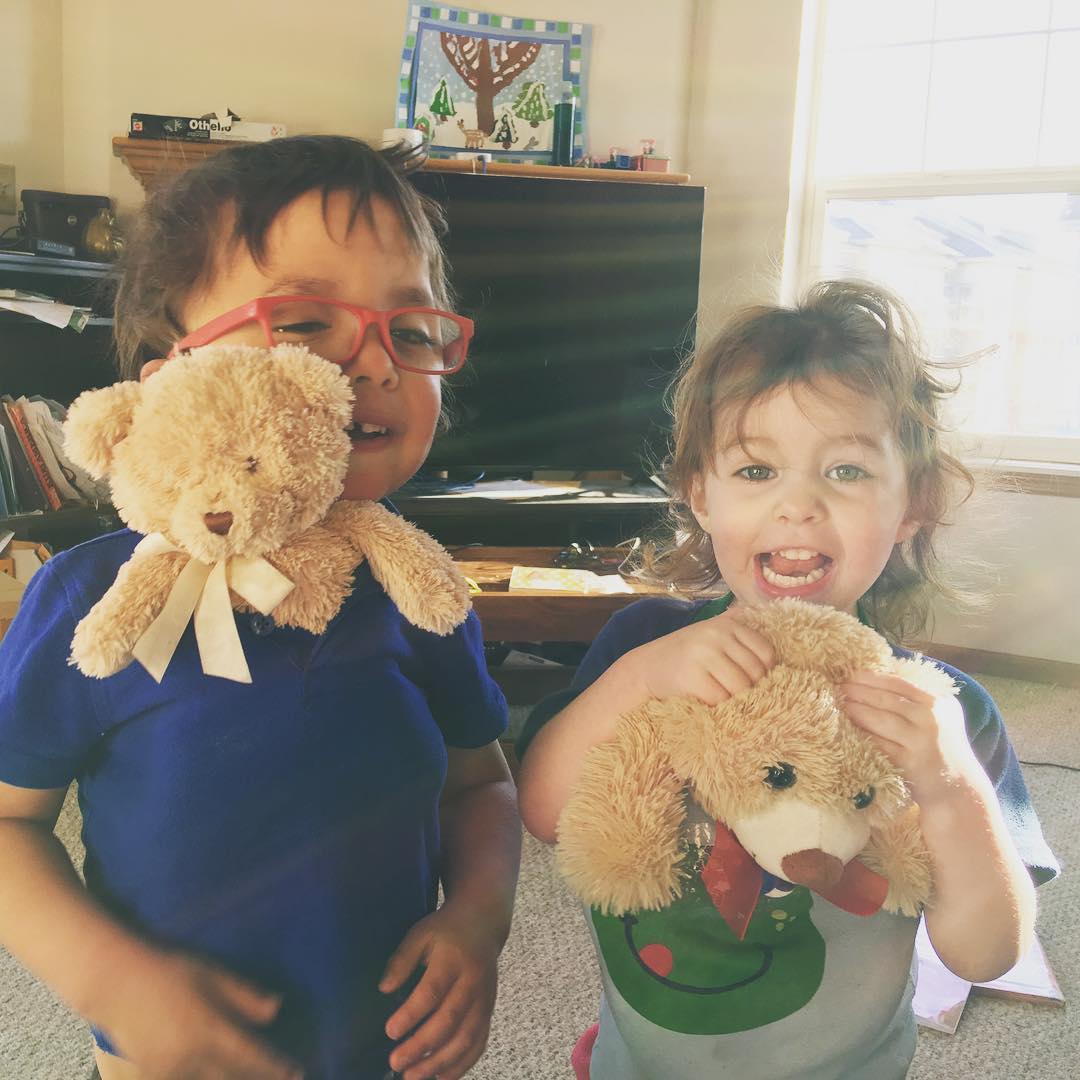 Three year old and two year old are laughing because they have teddy bears stashed in their shirts with their heads poking out the top.