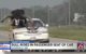 As the chyron suggests, there's a bull riding in the passenger seat of a white sedan. There's a gate on the side of the vehicle, and the right half of the roof and windshield appear to have been cut away.