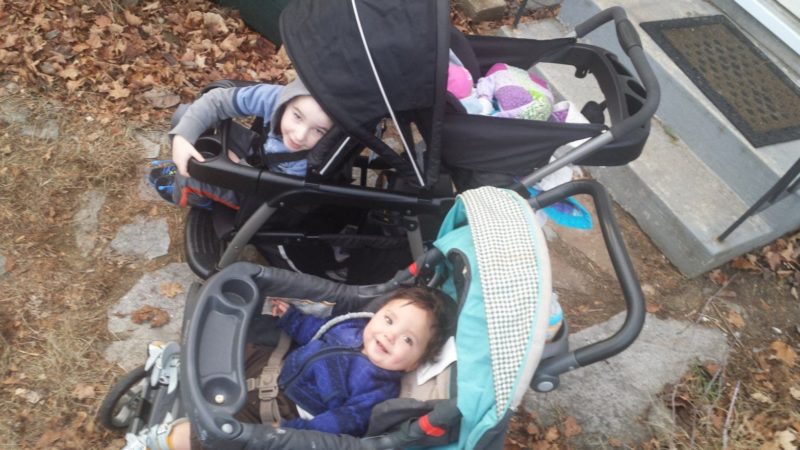 The Carlson Kids are in two strollers, smiling and preparing for a walk around a very non-snow covered driveway.