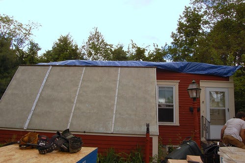 The red house with its top floor removed and a blue tarp over the top.