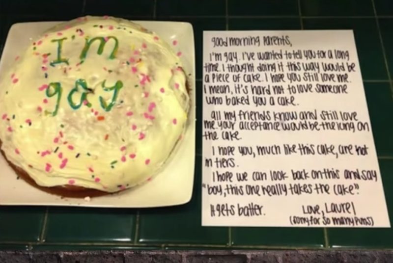 A sparkly cake with the words "I'm gay" in green letters on top. Next to it, a letter that reads, "Good morning parents, I'm gay. I've wanted to tell you for a long time. I thought doing it this way would be a piece of cake. I hope you still love me. I mean, it's hard not to love someone who baked you a cake. All my friends know and still love me. Your acceptance would be the icing on the cake. I hope you, much like this cake, are not in tiers. I hope we can look back on this and say, 'boy, this one really takes the cake.' It gets batter. Love, Laurel (sorry for so many puns)" 