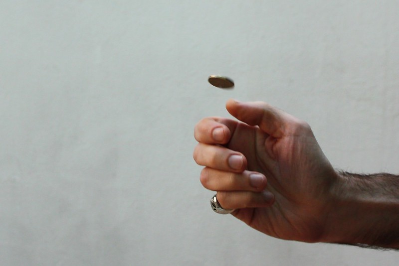A hand flips a coin into the air. (Photo by Nicu Buculei via Flickr/Creative Commons https://flic.kr/p/923r8Z)