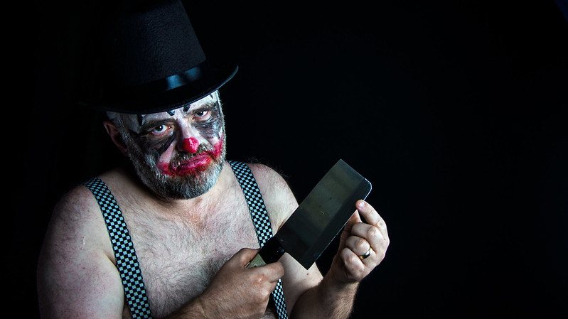 A sad looking clown in a top hat and suspenders holding a cleaver. (Photo by Stewart Black via Flickr/Creative Commons https://flic.kr/p/MwP7xj)