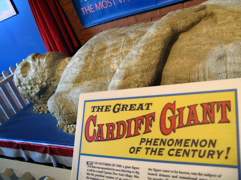 The statue known as the Cardiff Giant, on display at the Farmer's Museum in Cooperstown, NY. A sign in front reads "The great Cardiff Giant, phenomenon of the century!" (Photo by Keturah Stickann via Flickr/Creative Commons https://flic.kr/p/2vNeis)