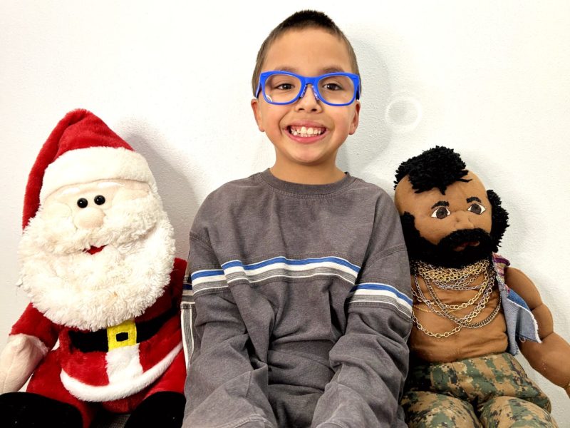 Eight year old smiles as he sits with our plush Santa Claus and Mr. T. 