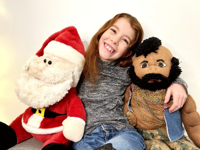 Seven year old smiles as she sits with our plush Santa Claus and Mr. T. 