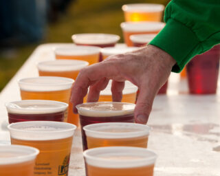 A hand reaches for a cup of beer on a table filled with beer cups. (Photo by Bill Dickinson via Flickr/Creative Commons https://flic.kr/p/c1Kmbh)