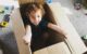 The 2 1/2 year old is smiling as she sits inside a cardboard moving box.