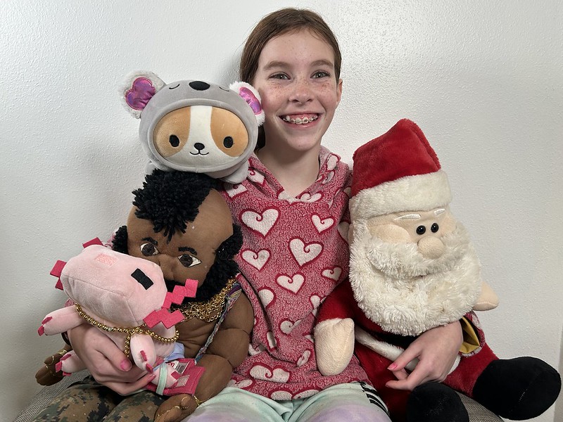 Ten year old poses with Santa and Mr. T, plus her Minecraft axolotl and a stuffed corgi wearing a koala suit.